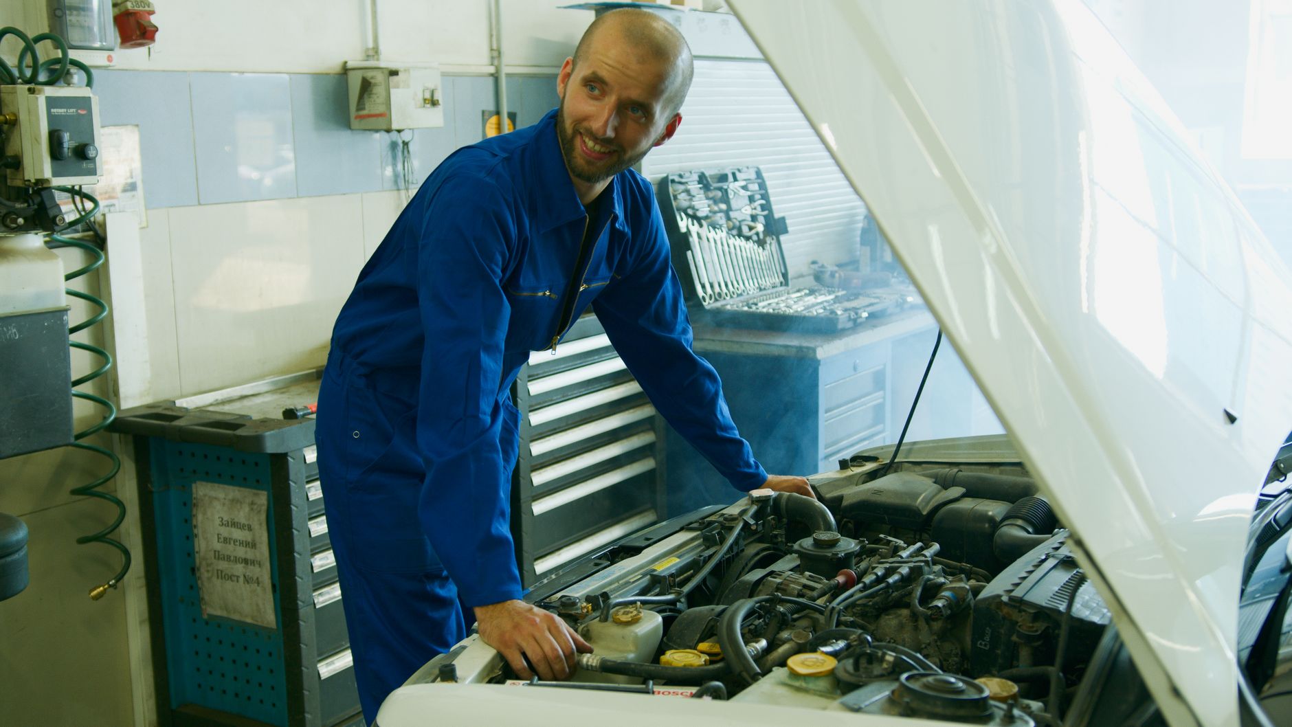 Smiling mechanic inspecting car engine in garage